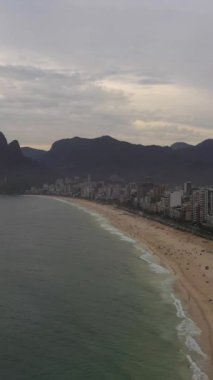 Rio de Janeiro Şehri. Sunset 'te Ipanema Sahili ve Atlantik Okyanusu. Hava görüntüsü. Brezilya. Drone plajın üzerinde ileri uçuyor. Dikey Video