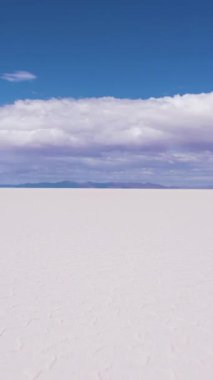 Güneşli bir günde Uyuni Tuz Düzlükleri. Salar De Uyuni. Hava görüntüsü. Altiplano, Bolivya. Kurak Mevsim. Altıgen Tuz oluşumları ve Çatlak desenleri. İHA alçaktan geriye doğru uçuyor. Geniş açı. Dikey Video