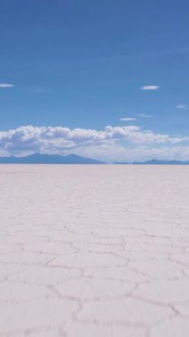 Güneşli bir günde Uyuni Tuz Düzlükleri. Salar De Uyuni. Hava görüntüsü. Altiplano, Bolivya. Kurak Mevsim. Altıgen Tuz oluşumları. İnsansız hava aracı alçaktan uçuyor. Geniş açı. Dikey Video