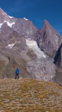 Mavi ceketli yürüyüşçü güneşli bir günde Mont Black Mountain 'a bakıyor. İtalyan Alpleri, İtalya. Hava görüntüsü. Yörüngede. Dikey Video