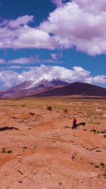 Gezgin Adam Ollague Volkanı ve Kaya oluşumlarına bakıyor. Bolivya 'da. Bulutlu Mavi Gökyüzü. Hava görüntüsü. İnsansız hava aracı alçaktan uçuyor. Solo seyahat. Dikey Video