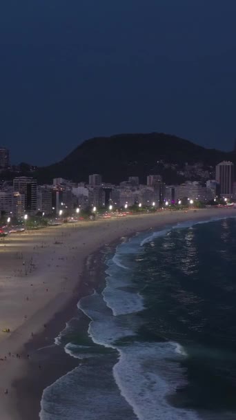夜のリオデジャネイロシティ コパカバーナビーチと大西洋 イブニング トワイライト ブルーアワー アリアルビュー ブラジル ドローン フライがビーチに向かって バーティカルビデオ — ストック動画