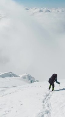 Dağcı Adam, Bulutların üstündeki Karlı Dağ yamacına inen Buz Baltası kullanıyor. Avrupa Alpleri. Dikey Video