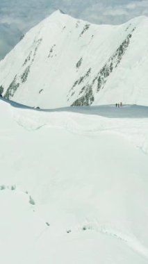 Güneşli bir günde Avrupa Alplerinde Karlı Dağ Zirvesi ve bir grup insan. Hava görüntüsü. Drone İleri Uçuyor, Eğil. Dikey Video