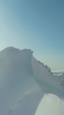 Güneşli bir günde Avrupa Alplerinde karla kaplı dağ. Hava görüntüsü. Drone ileri ve yukarı doğru uçuyor. Dikey Video