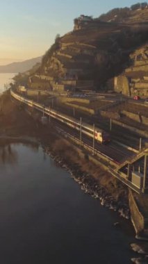 Tren Sunset 'te Cenevre Gölü kıyısında gidiyor. Teraslı üzüm bağları ve evler. İsviçre. Hava görüntüsü. Drone Treni Takip Ediyor. Dikey Video