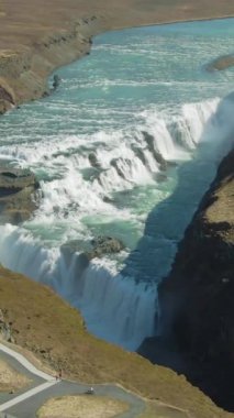 Gullfoss Şelalesi, yaz gününde. İzlanda. Hava görüntüsü. İnsansız hava aracı aşağıya doğru uçuyor, yukarı doğru. Dikey Video