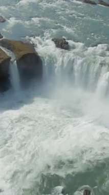Yaz güneşli gününde Godafoss Şelalesi. İzlanda. Hava görüntüsü. İHA ileri uçar, aşağı eğilir. Dikey Video