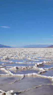 Güneşli günde Badwater Havzası. Su ve Mavi Gök ile Tuz Kabuğu oluşumları. Death Valley Ulusal Parkı. Kaliforniya, ABD. Hava görüntüsü. Dikey Video