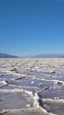 Güneşli günde Badwater Havzası. Su ve Mavi Gök ile Tuz Kabuğu oluşumları. Death Valley Ulusal Parkı. Kaliforniya, ABD. Hava görüntüsü. Yanlamasına hareket ediyor. Dikey Video