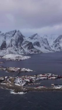 Kışın Hamnoy Köyü ve Dağları. Norveç Denizi ve Fırtınalı Gökyüzü. Moskenes, Lofoten Adaları, Norveç. Hava görüntüsü. Drone İleri Uçuyor, Eğil. Şutu göster. Dikey Video
