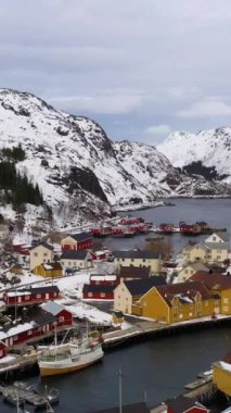 Kışın Nusfjord Balıkçılık Köyü, Rorbu, Fiyort ve Dağlar. Lofoten Adaları, Norveç. Hava görüntüsü. İnsansız hava aracı yukarı ve geri uçuyor. Dikey Video
