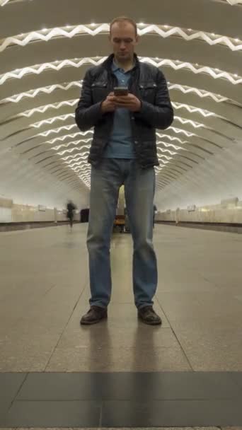 地下鉄駅にまだ立っている男のタイムラップと携帯電話の使用 人々の群れと通過列車 バーティカルビデオ — ストック動画