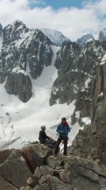 Peak of Rock 'ta iki dağcı. Karla kaplı dağlar. Hava görüntüsü. İnsan Dronie Yapar. Dikey Video