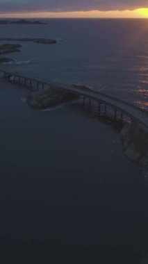 Norveç 'teki Atlantik Okyanusu Yolu' nda yaz günbatımında. Hava görüntüsü. Şutu göster. İHA ileri uçuyor, Kamera yukarı eğiliyor. Dikey Video