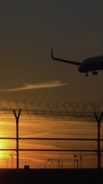 Sunny Sunset 'teki havaalanına iniş yapan uçağın silueti güneşe karşı. Ağır çekim. Dikey Video