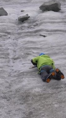Dağlardaki buz baltalarını kullanarak buz yamacında kayarken kendini durduran kramponlu dağcı adam. Ağır çekim. Dikey Video