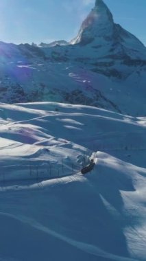 Matterhorn Dağı ve Güneşli Kış Gününde Tren. İsviçre Alpleri. İsviçre. Hava görüntüsü. Şutu göster. İHA ileri uçuyor, Kamera yukarı eğiliyor. Dikey Video