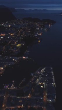 Norveç 'teki Alesund şehrini gece aydınlatmış. Hava görüntüsü. İHA ileri uçuyor, Kamera yukarı eğiliyor. Şutu göster. Dikey Video