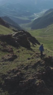Yürüyüşçü adam Sunny Summer Day 'de Dağ Zirvesi' nin tepesinde Yılan Yolu Geçidi 'nde duruyor. Drone yörüngede dönüyor. Hava görüntüsü. Atış ayarlanıyor. Kırgızistan. Dikey Video