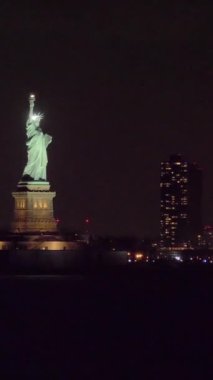 New York 'un Gece ve Binalarında Aydınlanmış Özgürlük Heykeli. Sudan görüntü. Yörüngede. Dikey Video