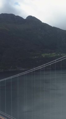 Norveç 'teki Eidfjorden' ın karşısındaki Hardanger Köprüsü yaz gününde. Fiyort ve Dağlar. Hava görüntüsü. Drone yörüngede dönüyor, Kamera aşağı eğiliyor. Dikey Video