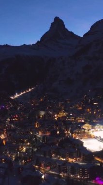Kışın Akşam Alacakaranlığı 'nda Zermatt Köyü ve Matterhorn Dağı. İsviçre. Hava görüntüsü. Drone geriye doğru uçuyor. Dikey Video