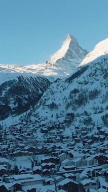 Güneşli Kış Günü 'nde Zermatt Köyü ve Matterhorn Dağı. İsviçre. Hava Aracı Atışı. Drone Yana ve Yukarı Uçuyor. Dikey Video
