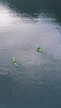 Geiranger Fjord 'un Turkuaz Suyu' nda iki yeşil kano. Norveç. Hava görüntüsü. Drone ileri uçuyor, Kamera aşağı eğiliyor. Dikey Video