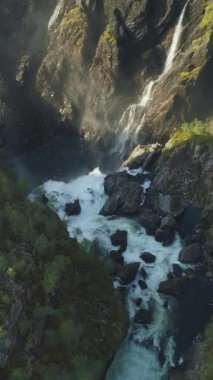 Voringfossen Şelalesi ve Norveç 'teki Yeşil Ağaçlı Kayalıklar Güneşli Yaz Günü' nde. Havadan Yukarıdan Aşağı Görünümü. Drone ileri uçuyor, Kamera aşağı eğiliyor. Dikey Video