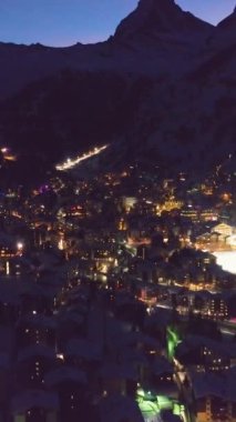 Gece Zermatt Köyü ve Matterhorn Dağı. İsviçre Alpleri, İsviçre. Hava görüntüsü. Şutu göster. İHA ileri uçuyor, Kamera yukarı eğiliyor. Dikey Video