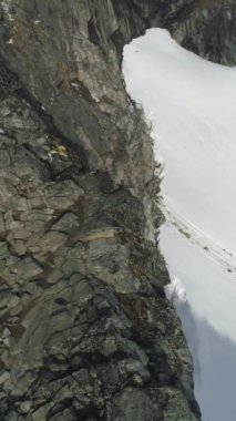 Yürüyüşçü Adam, Norveç 'in Karlı Dağları' ndaki Kayalıklar 'da Yayan Polonyalıları kullanarak Yürüyüş ve İniş yapıyor. Hava görüntüsü. Drone yörüngede dönüyor. Dikey Video