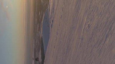 İnsanlar Sunny Winter Sunset 'te kayak ve kar kayağı yapıyorlar. Çerçevedeki Güneş. Hava görüntüsü. İnsansız hava aracı Yanlamasına uçuyor. Çekim.. Dikey Video Kuruluyor