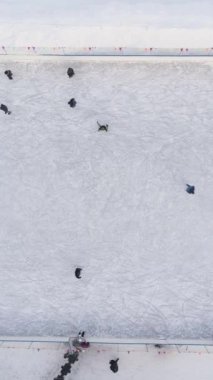 İnsanlar güneşli bir günde buz pateni pistinde kayıyorlar. Havadan yukarıdan aşağıya doğru. Çekim başlıyor. Drone aşağıya doğru uçuyor. Dikey Video