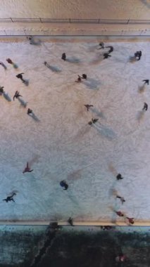 Bir grup insan akşamları aydınlık buz pistinde paten kayıyor. Havadan yukarıdan aşağıya doğru. Çekim başlıyor. Dikey Video