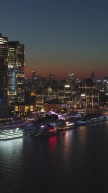 Akşam Alacakaranlığı 'nda Şangay Skyline' ı aydınlattım. Puxi Bölgesi ve Huangpu Nehri. Hava görüntüsü. Drone Yanlamasına Uçuyor ve Yükseliyor. Dikey Video