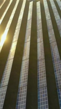Gün batımında büyük mavi fotovoltaik güneş panelleri alanı. Güneş ışığı yansıması. Hava görüntüsü. Yanlamasına sağa doğru uçuyor. Çekim başlıyor. Dikey Video