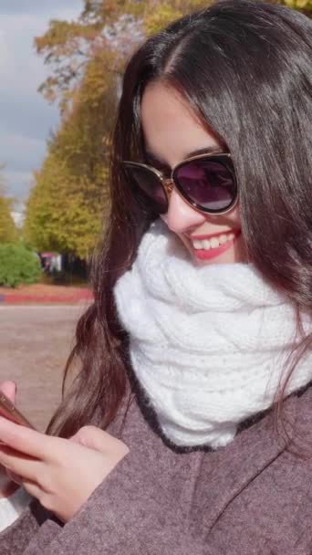 在城市公园里 年轻美丽的黑发女子 戴着墨镜 卷曲长发 正在使用智能手机 慢动作垂直录像 — 图库视频影像