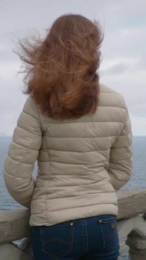 Genç Kadın Rüzgarlı Gün 'de Uçurumlara ve Denize Bakıyor. Dikey Video