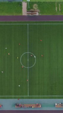 Yeşil futbol sahasının üzerinde uçuyor. Futbol oynayan oyuncular. Hava dikey üst görünümü. Dikey Video
