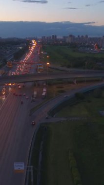 Şehirdeki bir otoyolda gece vakti trafik vardı. Şehir manzarası. Geri geri uçmak. Hava görüntüsü. Dikey Video