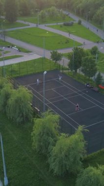 Green City Park 'ta tenis oynayan oyuncuların etrafında uçmak. Kaldırımda yürüyen insanlar. Hava görüntüsü. Dikey Video