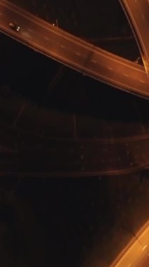 İnsansız hava aracı aydınlanmış karmaşık kavşağın üzerinde uçuyor. Geceleri araba trafiği. Havadan dikey çekim. Dikey Video