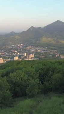 İnsansız hava aracı sabah dağın yeşil ormanlık yamacında uçuyor. Arka planda yeşil dağlar var. Dikey Video