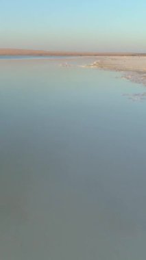 Sabahları tuzlu göl suyunun üzerinde tuzlu su birikintileriyle hızla uçan drone. Hava görüntüsü. Dikey Video