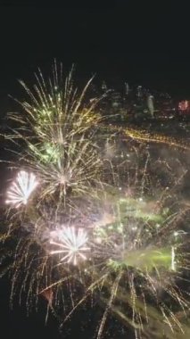 Aydınlanmış şehirde gece tatilde renkli havai fişekler. Kamera aşağı eğiliyor. Hava görüntüsü. Dikey Video
