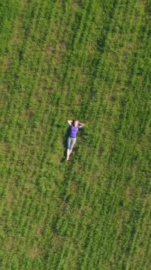 Genç kadın büyük yeşil çimlerde dinleniyor. Drone dönüyor ve yukarı doğru uçuyor. Hava görüntüsü. Dikey Video