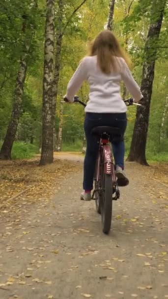 若い女性が公園で自転車に乗っている 秋と秋の黄色い葉 ステディカムショット スローモーション バーティカルビデオ — ストック動画