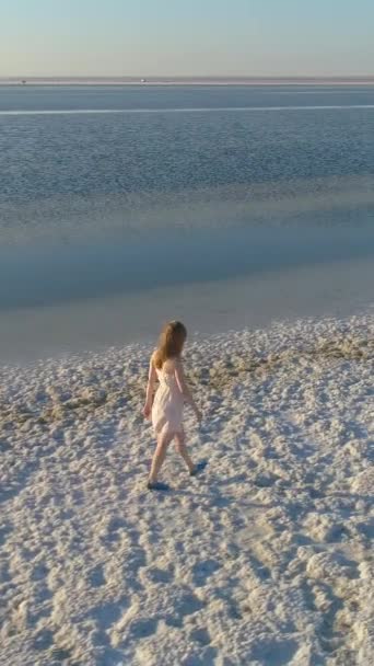 身穿白衣的年轻寂寞女子正沿着盐湖岸散步 空中风景 垂直录像 — 图库视频影像