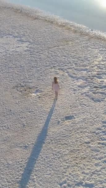 身穿白衣的年轻女子正在盐湖城的白岸上散步 空中俯瞰 垂直录像 — 图库视频影像